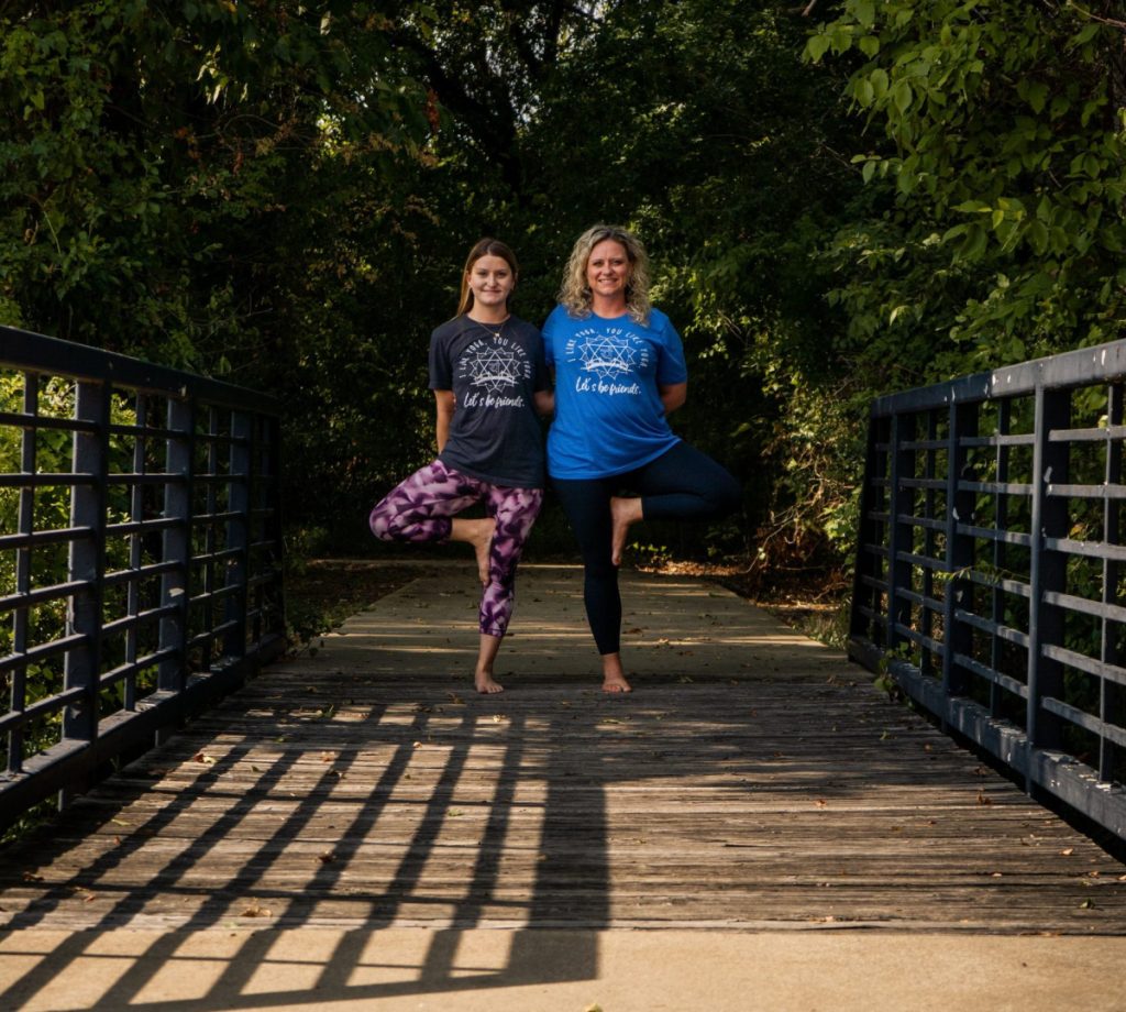 two woman standing in tree pose outside